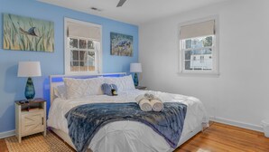 A bedroom with a bed, two bedside tables, two lamps, a ceiling fan, and two windows. - New, Walk to Beach, Game Room, Fire Pit, King Beds (Norfolk)