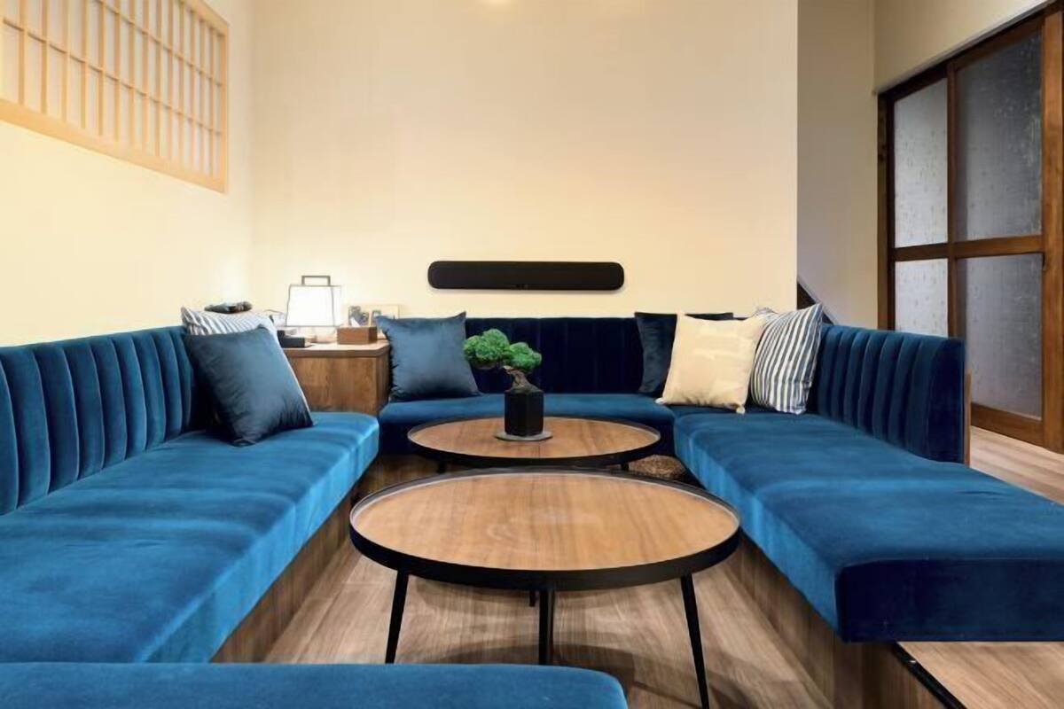 A modern living room with a blue sofa set, two round wooden tables, and a small potted plant.