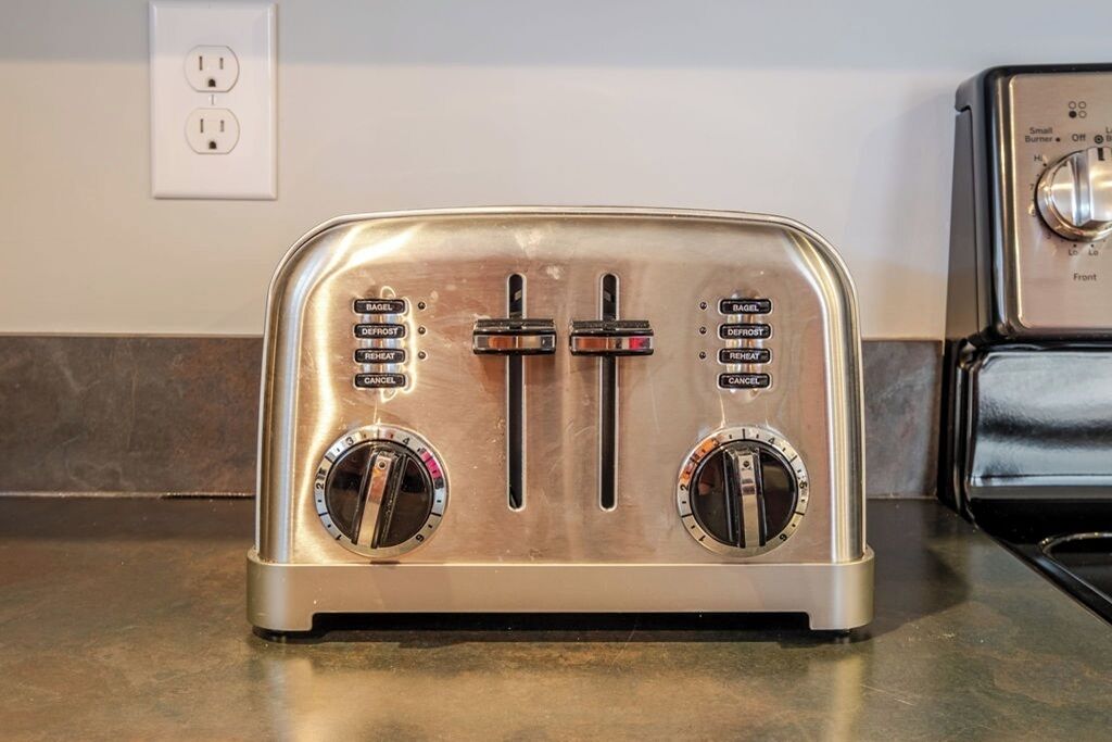 A stainless steel toaster with two slots and two control knobs on a kitchen countertop.