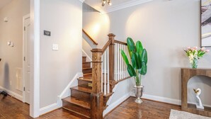 A wooden staircase with white railings, a potted plant, and a framed artwork on the wall.