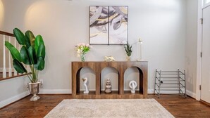 A room with a wooden console table, a large abstract painting, a potted plant, and a metal drying rack.