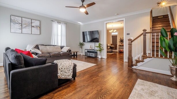A living room with a dark-colored sofa, a wooden floor, a ceiling fan, and a staircase leading to an upper level.