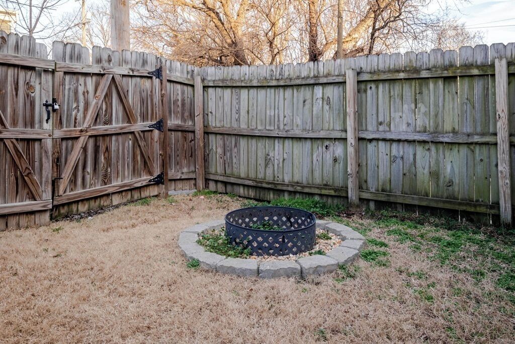 A backyard with a wooden fence, a circular garden bed with plants, and a dry grassy area.