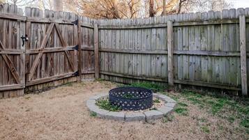 A backyard with a wooden fence, a circular garden bed with plants, and a dry grassy area.