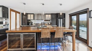 Une cuisine moderne dotée d’un îlot central, de tabourets de bar et offrant une vue sur l’extérieur grâce à de grandes fenêtres.