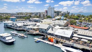 Un port de plaisance où sont amarrés de nombreux bateaux, un restaurant au bord de l’eau appelé « James Squire », et en arrière-plan, des immeubles urbains et un ciel dégagé.