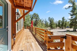A wooden deck with a railing, a red umbrella, and a view of trees and a clear sky. - Spacious & Cozy Mountain House in Fairplay (Fairplay)