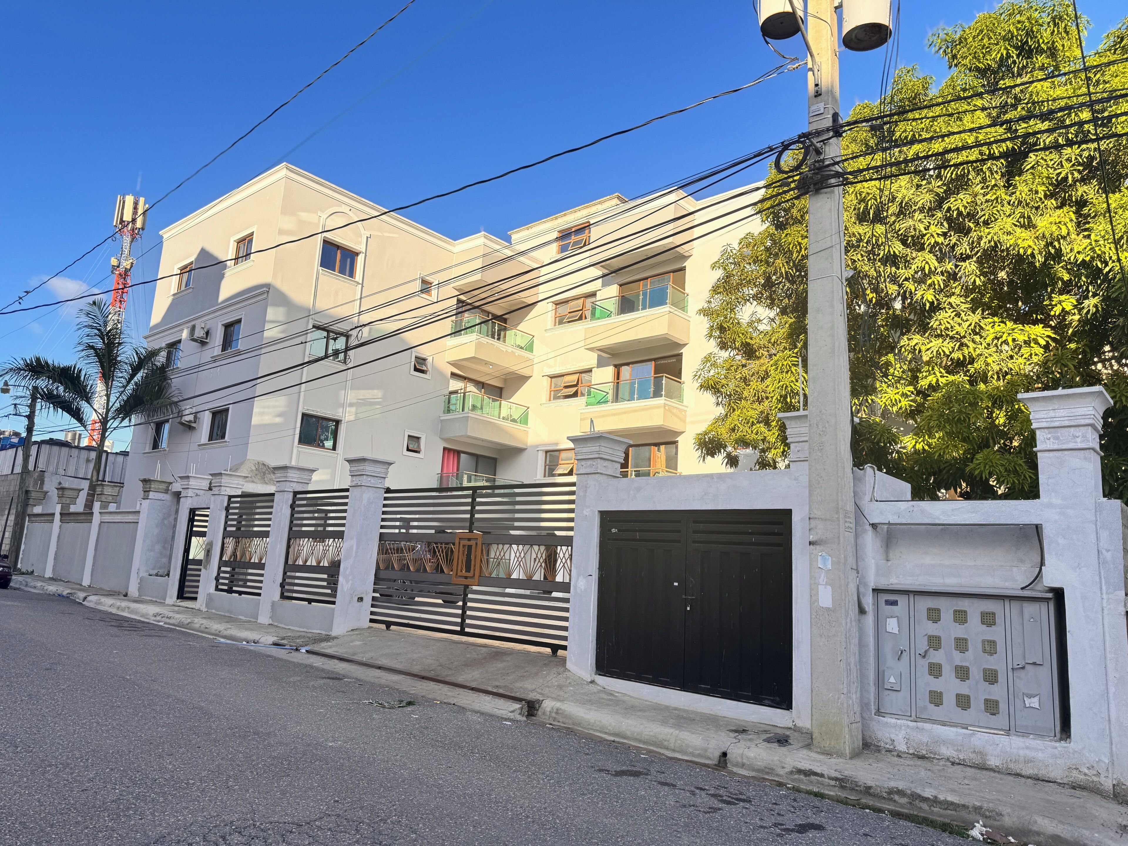 A multi-story residential building with a gated entrance, balconies, and a clear sky.