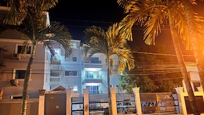 A nighttime view of a multi-story building with balconies, palm trees, and a gated entrance. - Enjoy Huge 4 Bedrooms and 3 Bathrooms (Santiago de los Caballeros)