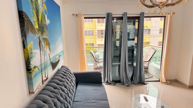 A modern living room with a large sofa, a glass coffee table, and a painting of a tropical scene. - Enjoy Huge 4 Bedrooms and 3 Bathrooms (Santiago de los Caballeros)