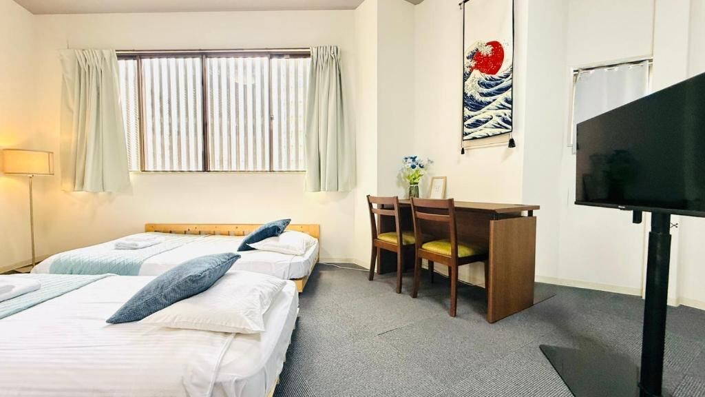Habitación de hotel con dos camas, un escritorio, una silla, un televisor y una ventana con cortinas.