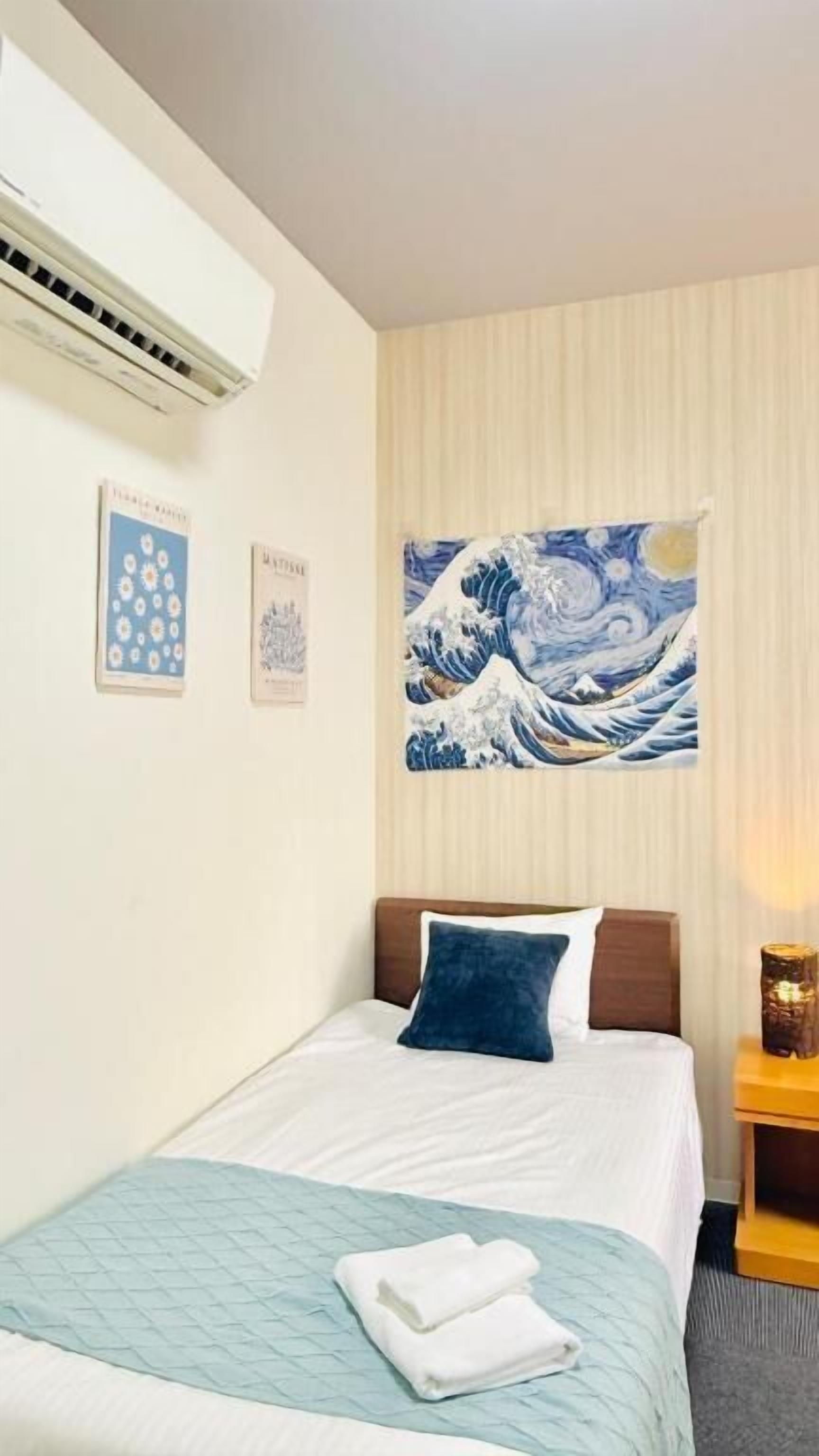 A hotel room with a bed, a painting of waves, and a nightstand with a lamp.