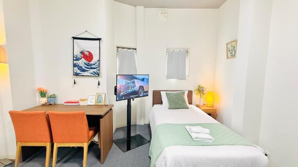 Una habitación de hotel con una cama, un escritorio con sillas, un televisor y un cuadro colgado en la pared.