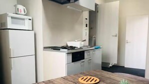 Une cuisine compacte équipée d’un four à micro-ondes, d’une cuisinière et de placards. On y trouve une table en bois avec un dessous de verre et deux plantes en pot.