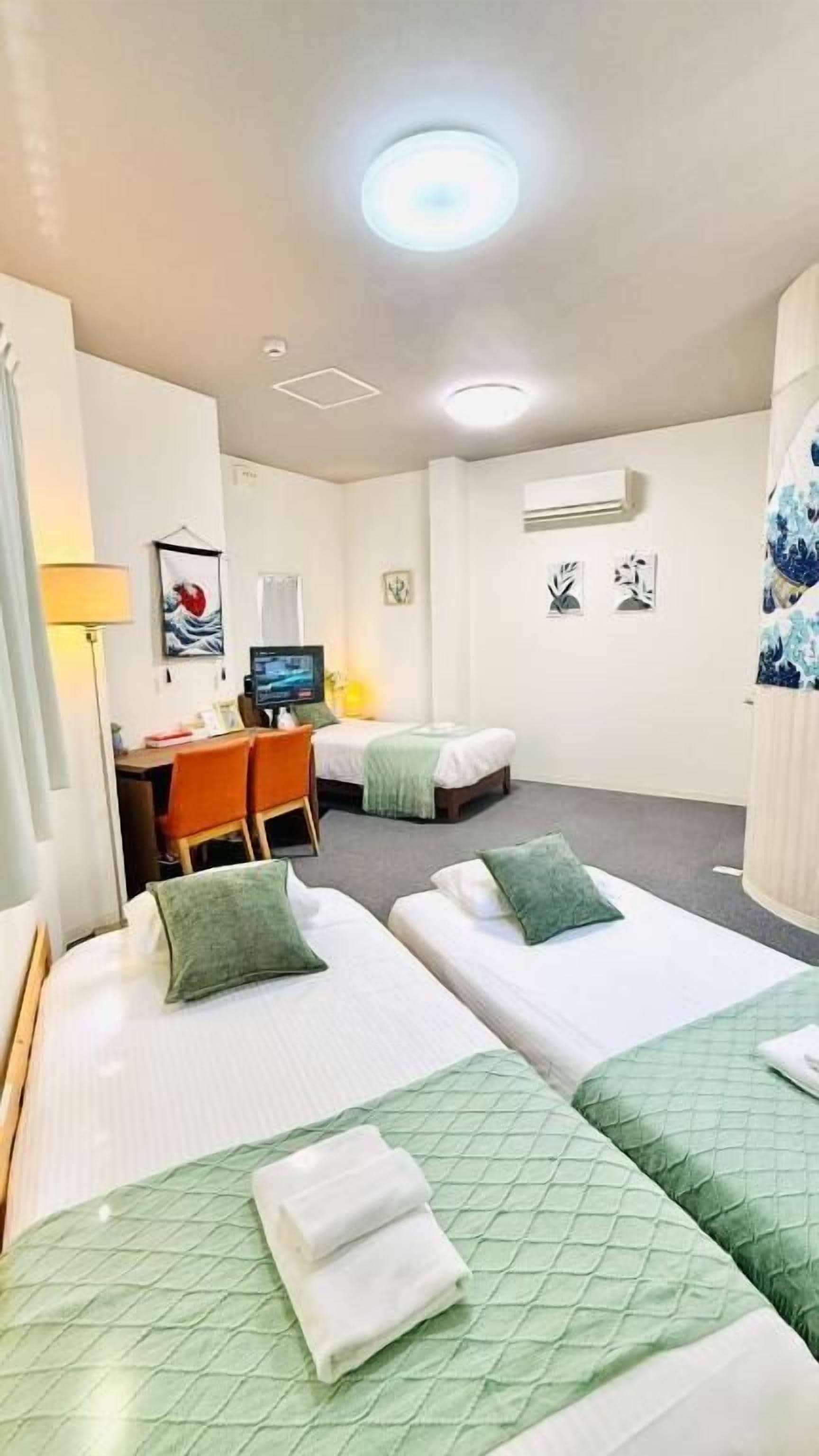 A hotel room with two beds, a desk, a chair, and a TV.