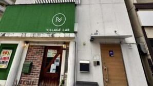Un immeuble de grande hauteur dont le rez-de-chaussée présente une façade verte avec l’inscription « VILLAGE LAB ».