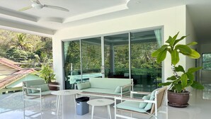 Un salon moderne avec un mur en verre, des meubles blancs et une grande plante en pot.