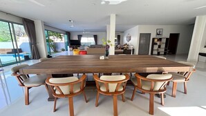 Un vaste espace dédié à la salle à manger, avec une grande table en bois entourée de six chaises, un téléviseur et un canapé en arrière-plan.