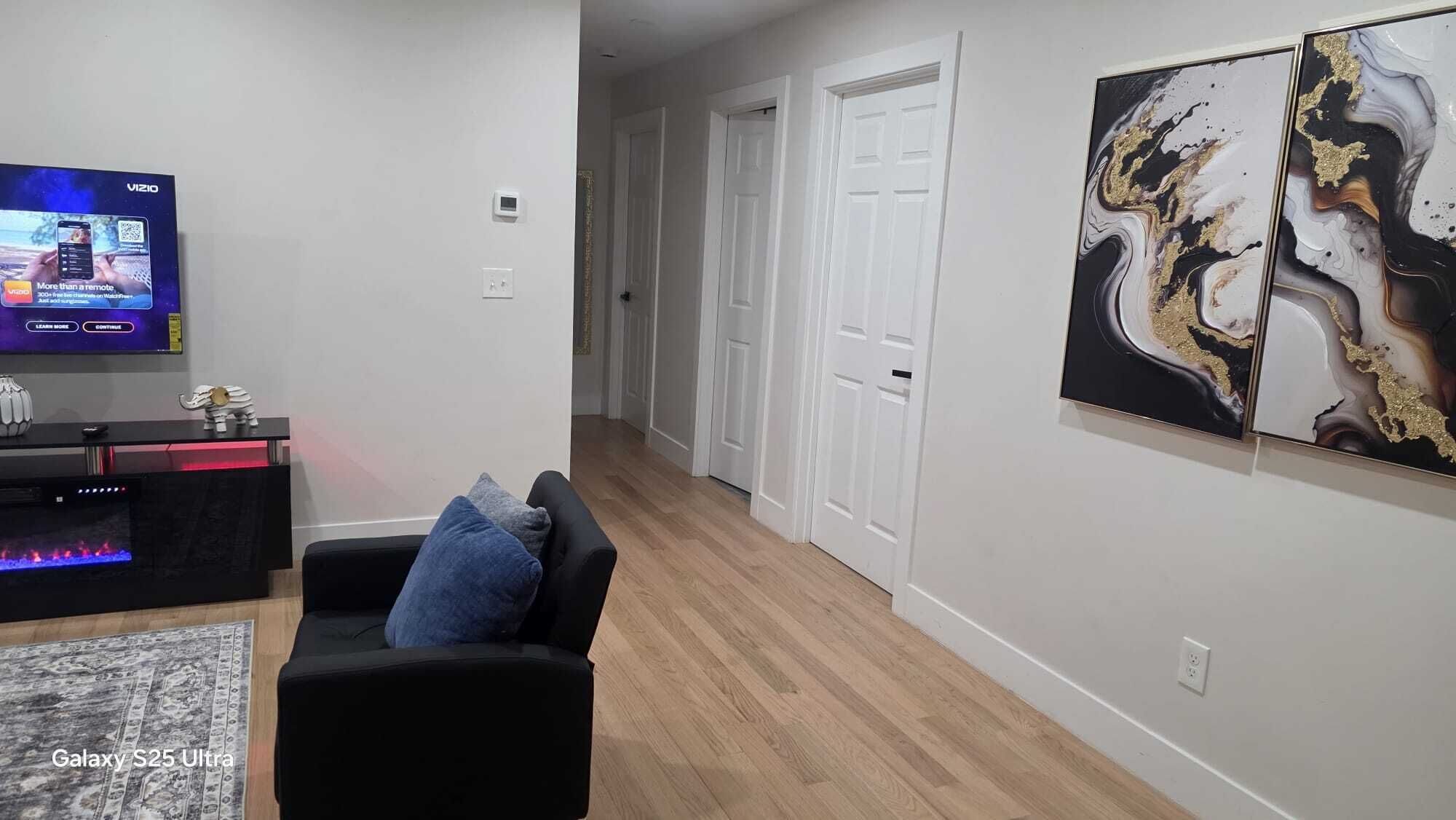 A modern living room with a Galaxy S25 Ultra TV, a black sofa with a blue pillow, and a marble-patterned rug.