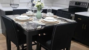 Una cocina moderna con armarios oscuros, una mesa de comedor de mármol y sillas tapizadas en negro.