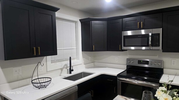 Una cocina moderna con armarios oscuros, un microondas de acero inoxidable, una estufa negra y una encimera blanca.