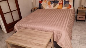 A bedroom with a bed, a wooden nightstand, a bedside table, a wooden bench, and a large window with a wooden frame. - city-centre apartment close to historic sites and shops (Nîmes)