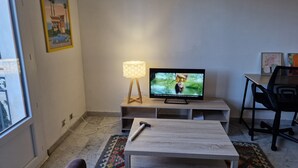 A living room with a TV, a lamp, a table, and a chair. - city-centre apartment close to historic sites and shops (Nîmes)