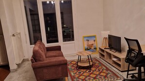 A living room with a brown sofa, a small wooden coffee table, a TV on a wooden stand, and a black office chair. - city-centre apartment close to historic sites and shops (Nîmes)