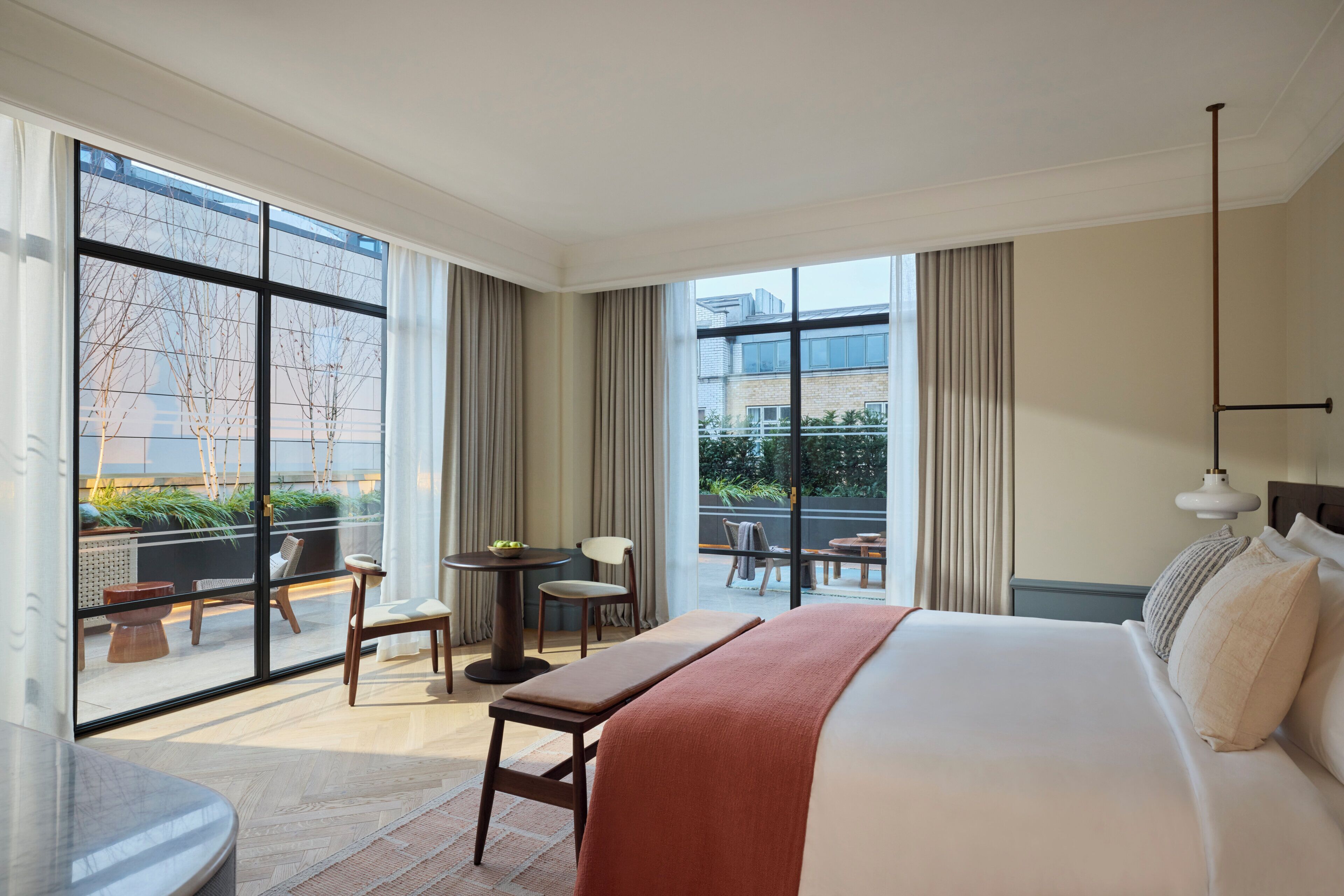 A hotel room with a large bed, a dining table, chairs, and a view of the outside.
