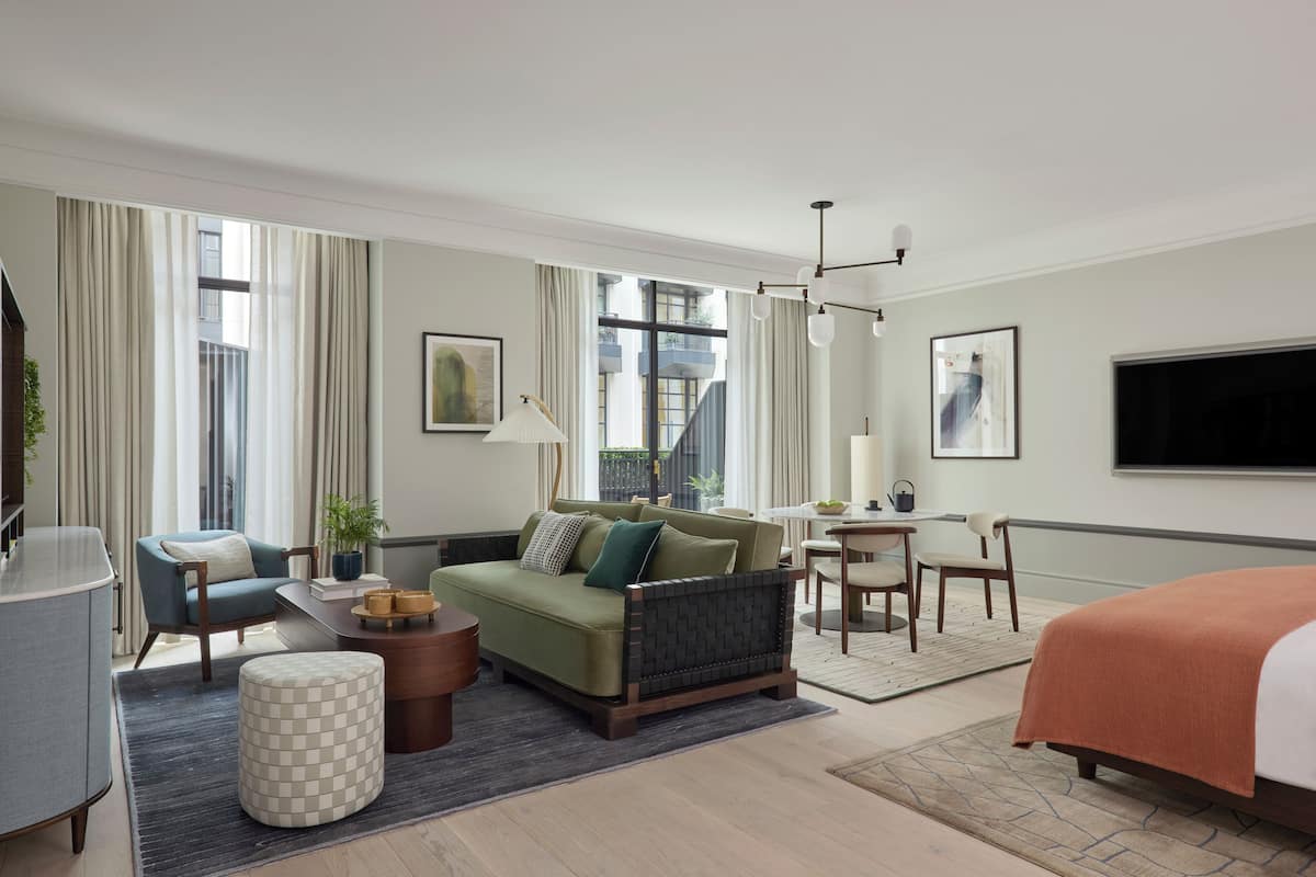 A hotel room with a sofa, armchair, dining table, and a bed.