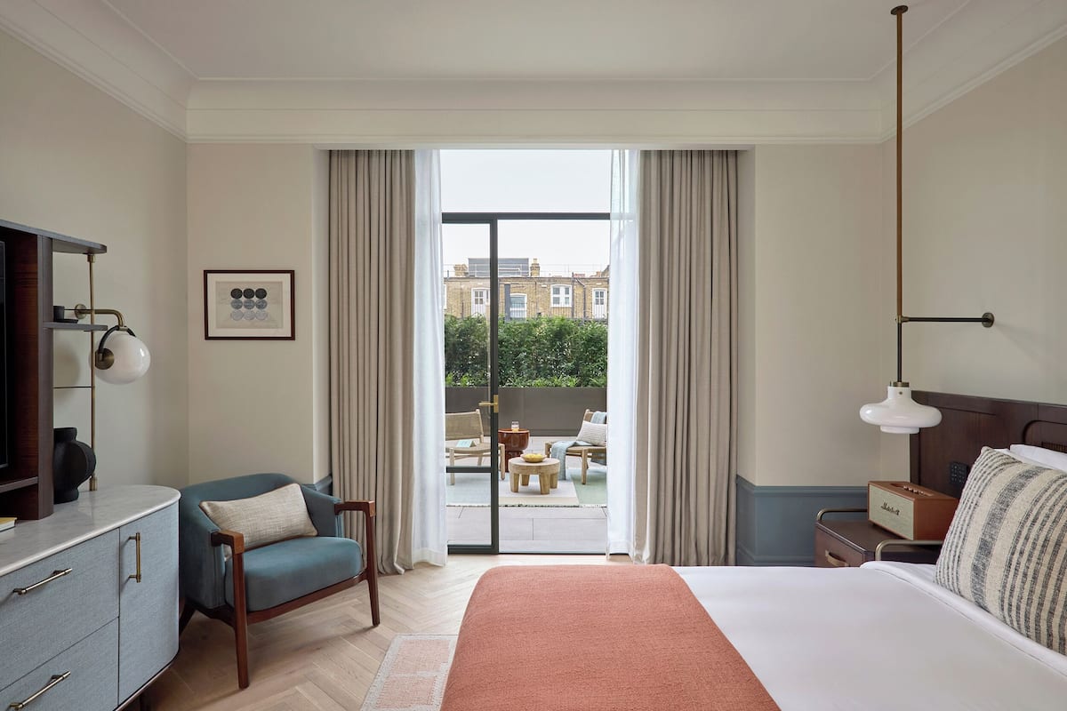 A hotel room with a bed, a desk, a chair, a TV, and a balcony with outdoor furniture.