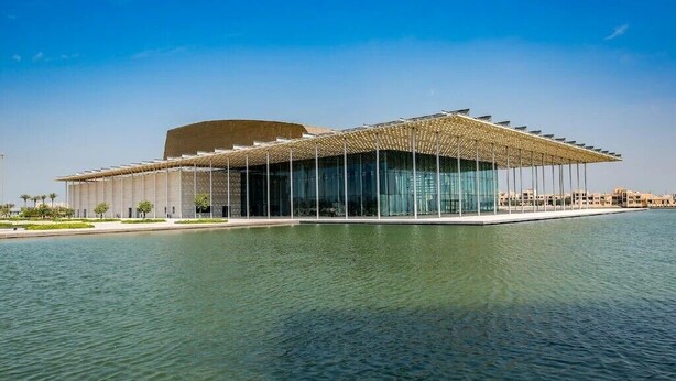 A modern building with a curved roof and a glass facade, situated by a body of water. - Mirador Hotel (Manama)