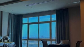 A hotel room with a large window, a dining table, and a chandelier. - Mirador Hotel (Manama)