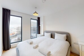 Ein modernes Hotelzimmer mit einem großen Bett, zwei Nachttischen, einem Fenster mit Vorhängen und Blick auf die Stadt.