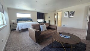 Een slaapkamer met een bed, een bruine bank, een ronde salontafel en een raam.