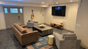 Een moderne woonkamer met een bank, fauteuils, een salontafel, een televisie en een gitaar.