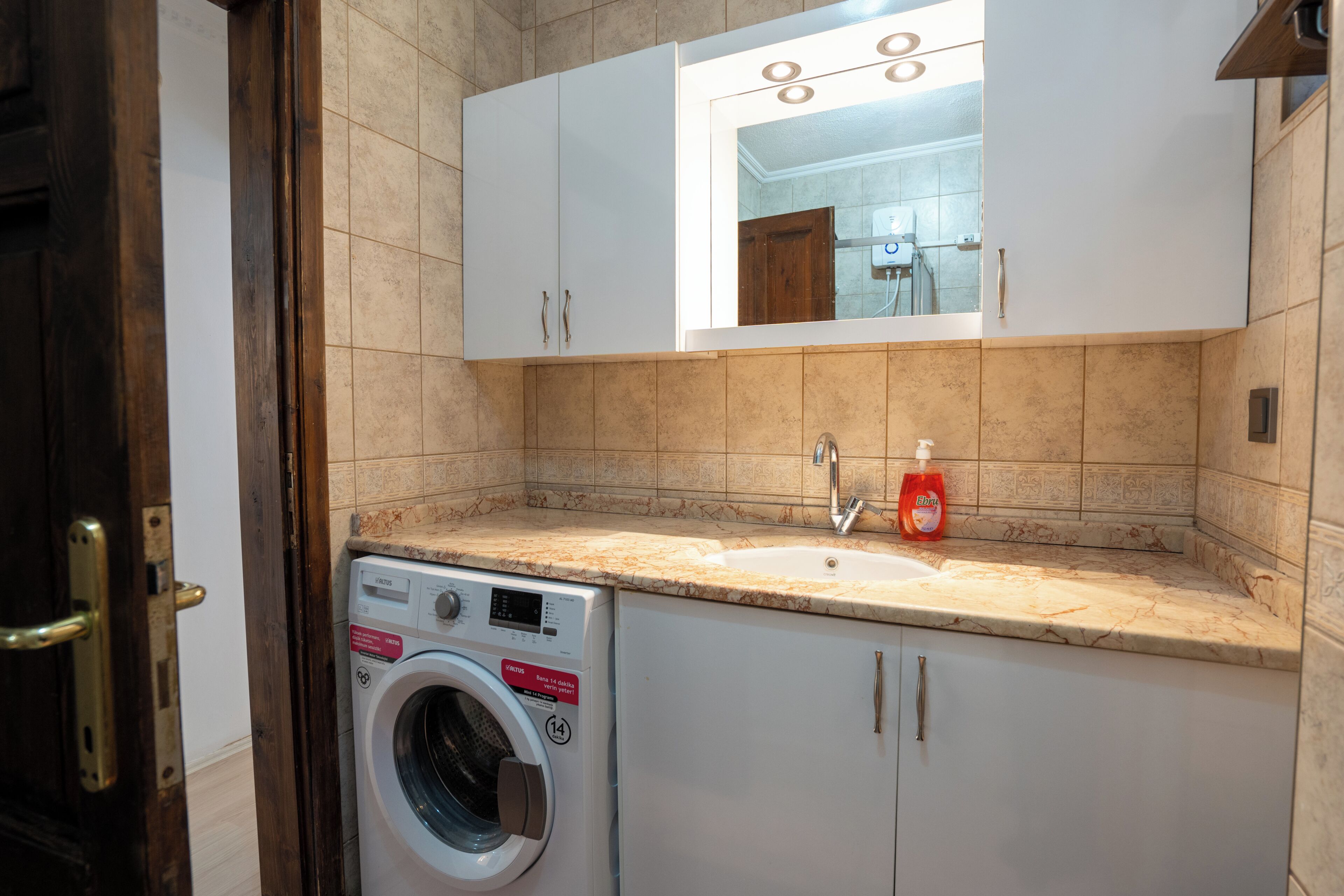 A compact bathroom with a washing machine, a sink, and a mirror above it.