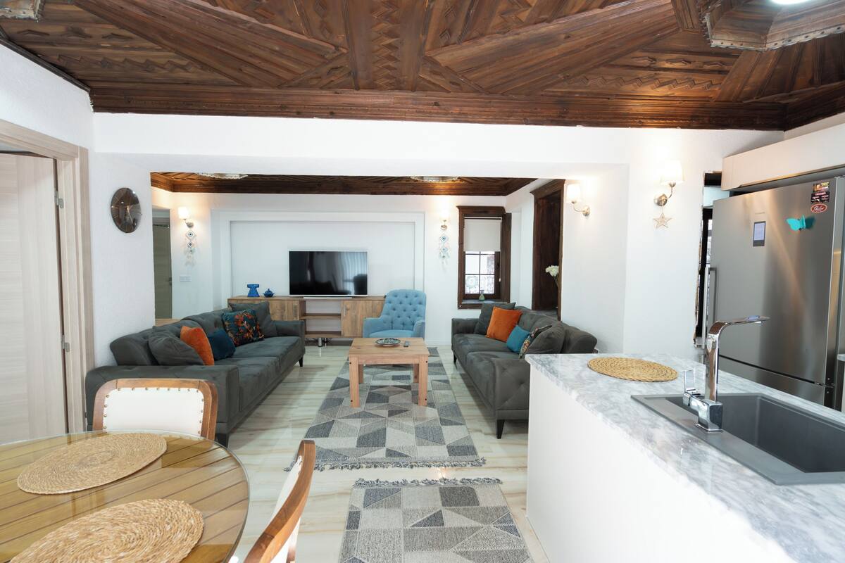 A living room with sofas, a coffee table, a TV, and a kitchen area with a refrigerator.