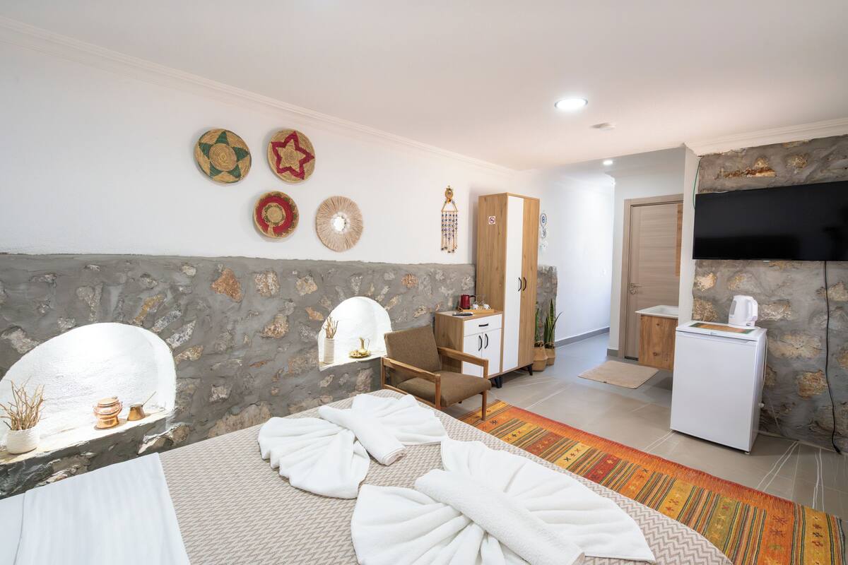 A hotel room with a bed, a wooden wardrobe, a television, and a stone wall.
