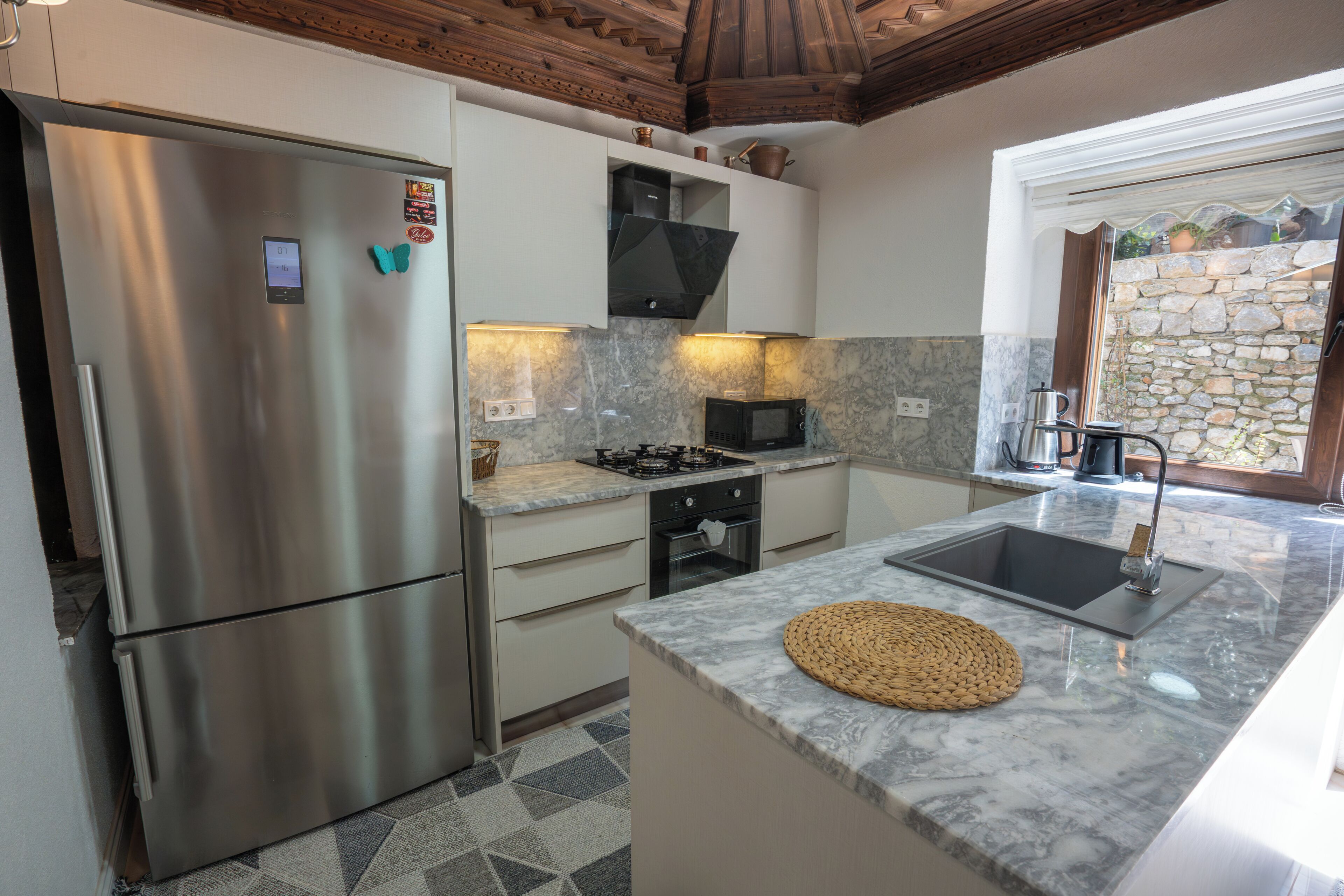 A modern kitchen with stainless steel appliances, a granite countertop, and a stone wall.