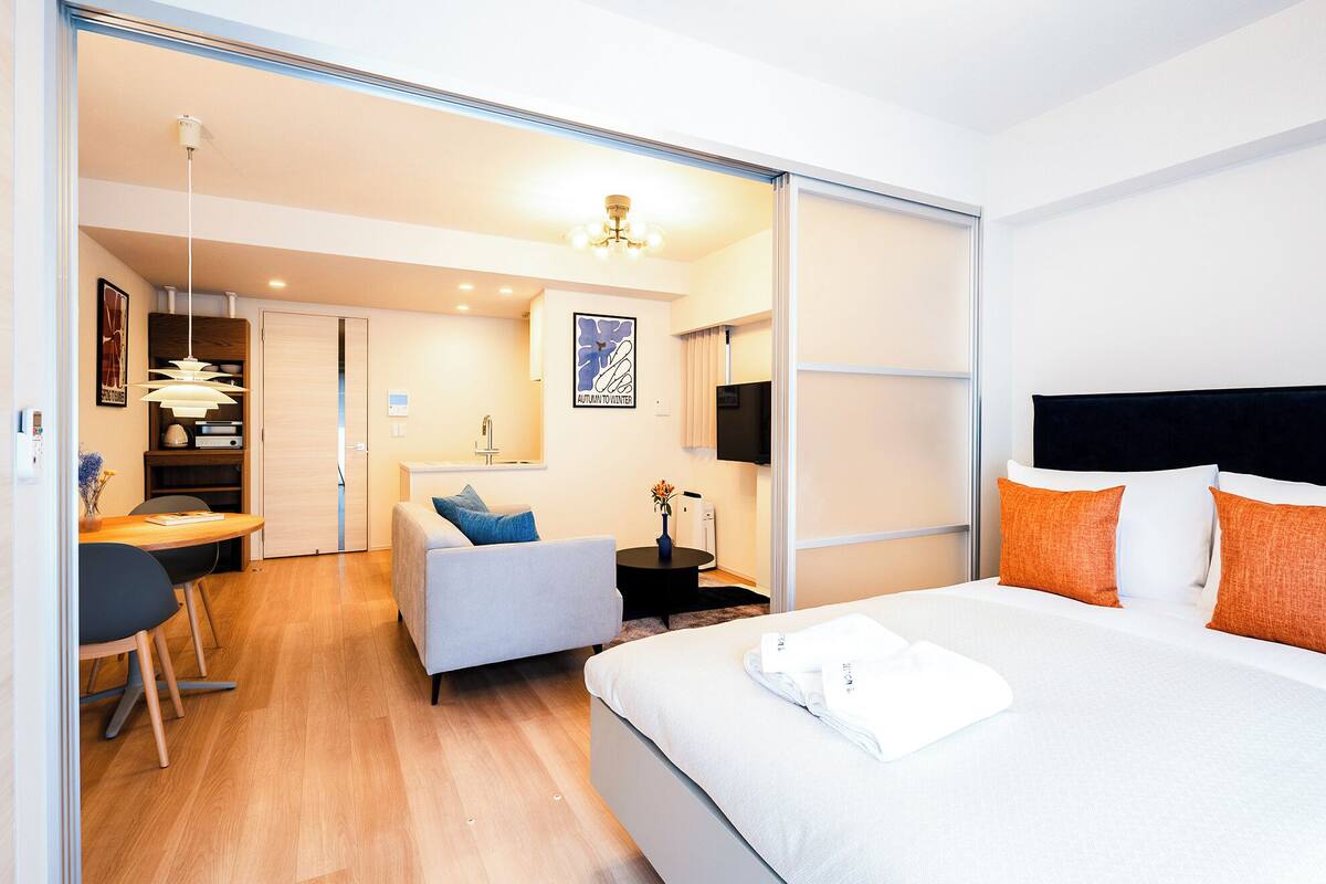 A modern hotel room with a bed, a desk, a chair, and a sofa.