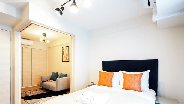 A modern bedroom with a bed, bedside table, and a seating area with a sofa and chairs. - Section L Residence Shibuya (Tokyo)