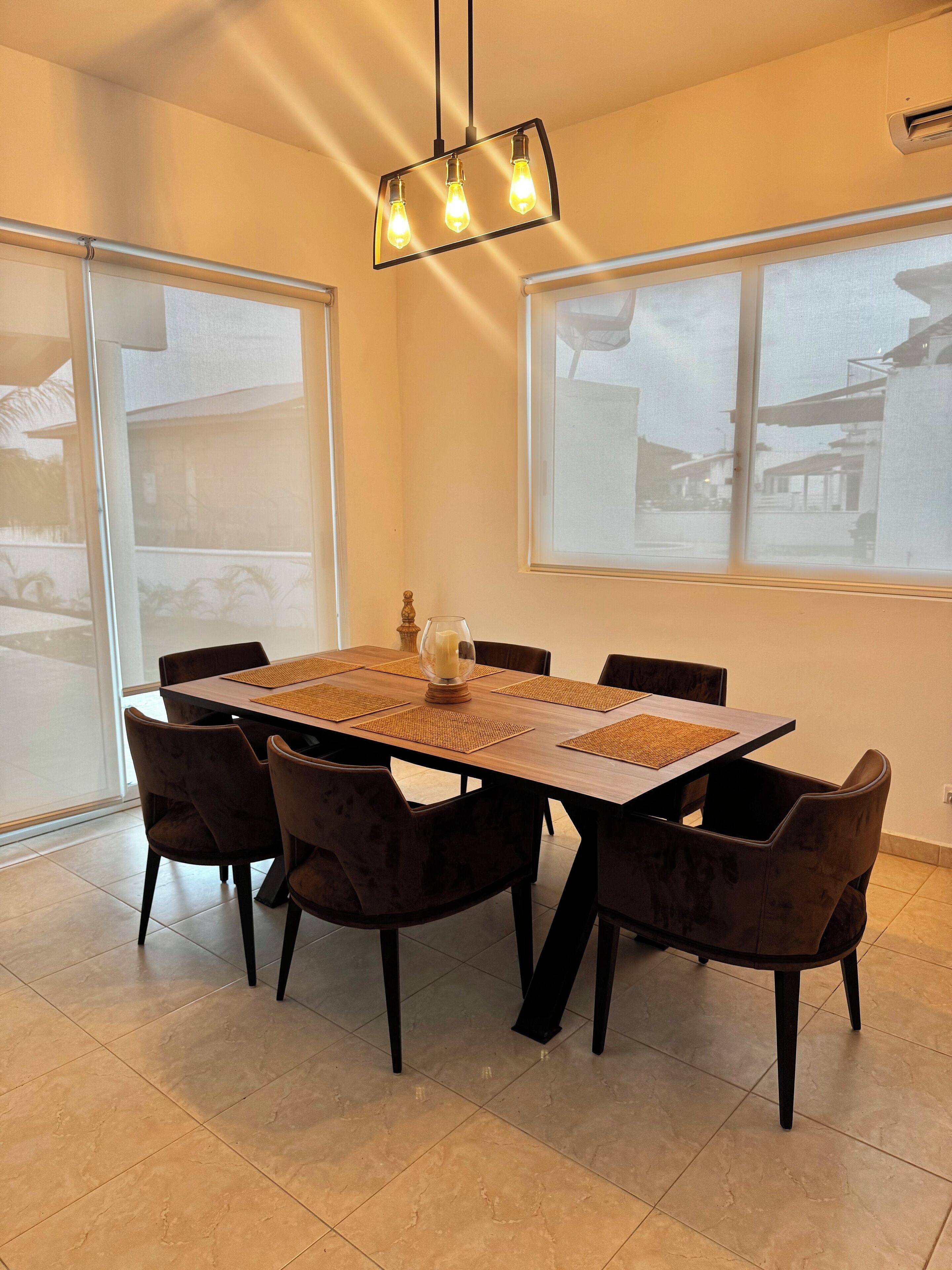Een eetgedeelte met een rechthoekige tafel, zes stoelen en een moderne hanglamp.