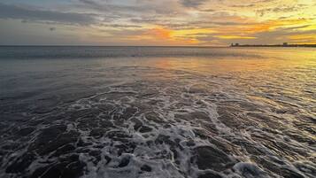 Una playa con olas y una puesta de sol al fondo.