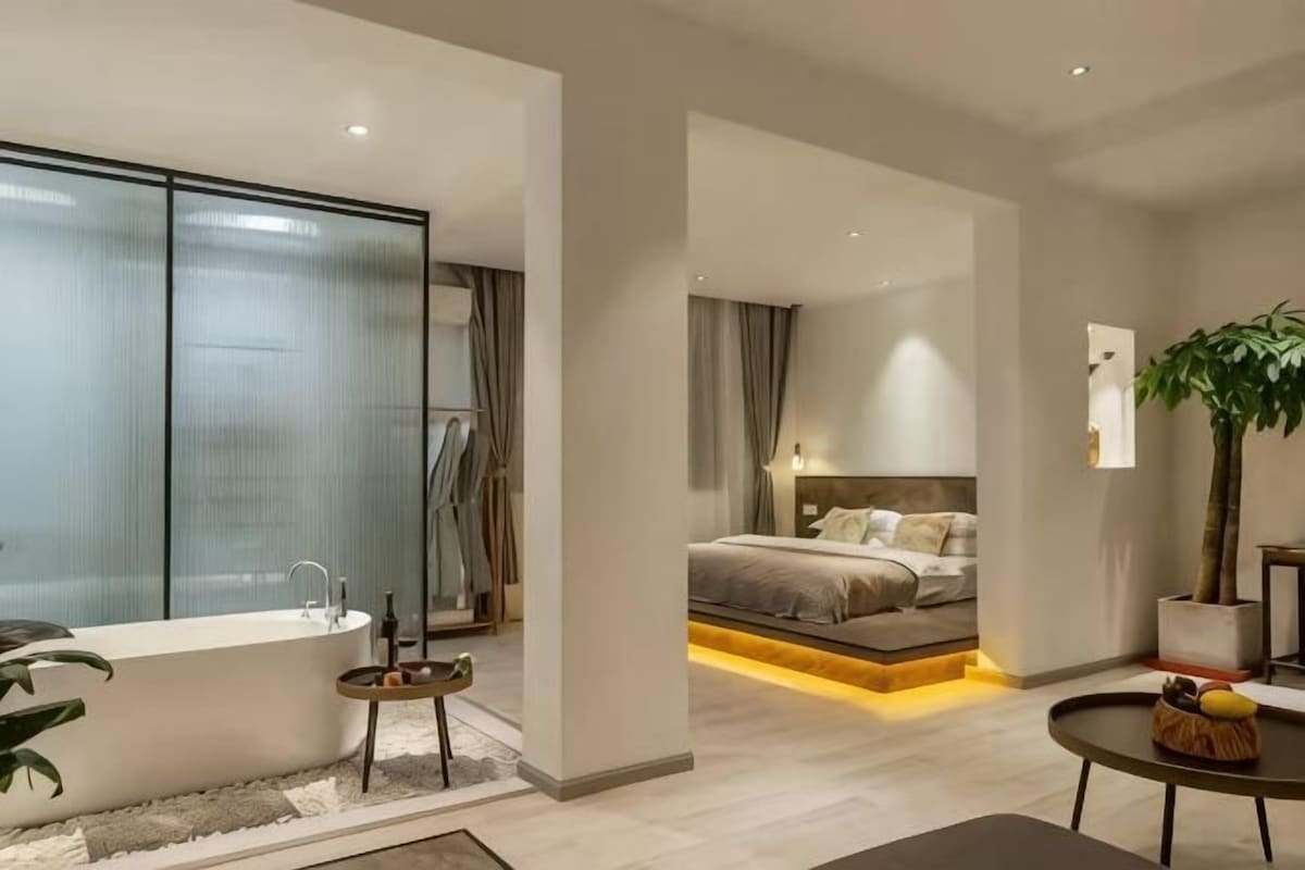 A modern bedroom with a large bed, a separate bathroom, and a small seating area.