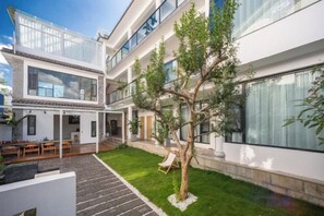 A modern multi-story building with a courtyard featuring a tree, outdoor seating, and a well-maintained lawn. - Dali Ancient City Bantian Homestay (Dali Ancient City Branch) (Dali)