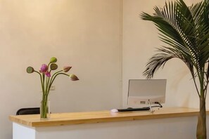 A reception desk with a computer monitor, a vase with flowers, and a potted plant. - Dali Ancient City Bantian Homestay (Dali Ancient City Branch) (Dali)