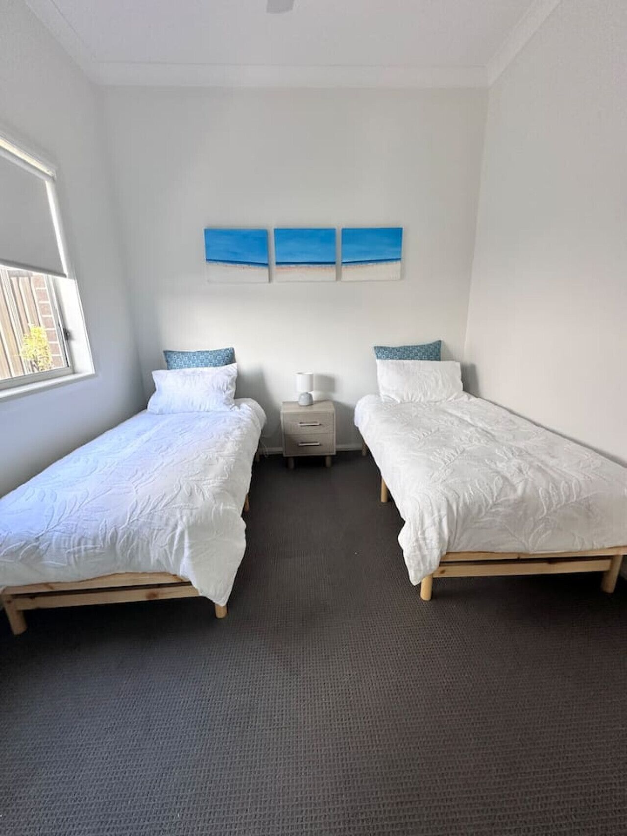 A bedroom with two single beds, a nightstand, a lamp, and a window.