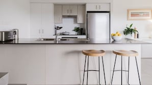 Una cuina moderna amb armaris blancs, electrodomèstics d'acer inoxidable i una illa central amb tamborets.