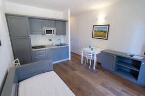 A compact kitchen with grey cabinets, a microwave, a sink, and a dining area with a table and chairs. - Elbamar Lacona 2 - Elbamar Lacona 2 - Bilo 4 Classic (Capoliveri)
